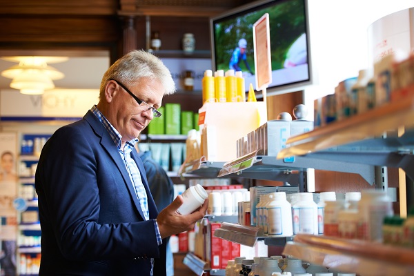 Older adult man reading back of supplement bottles on the shelf of a store
