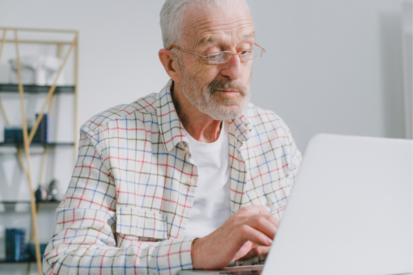 Older adult man sitting at laptop with look of contemplation