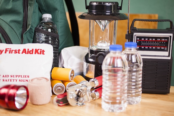 Emergency preparedness supplies. A large pile of supplies to be used in case of a natural disaster (hurricane, flood, earthquake, etc.) including: flashlight, backpack, batteries, water bottles, first aid kit, lantern, radio, can opener, mask. No people.