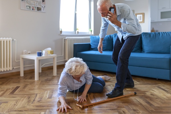 Senior wife sitting on floor while retired husband talking on smartphone calling an ambulance